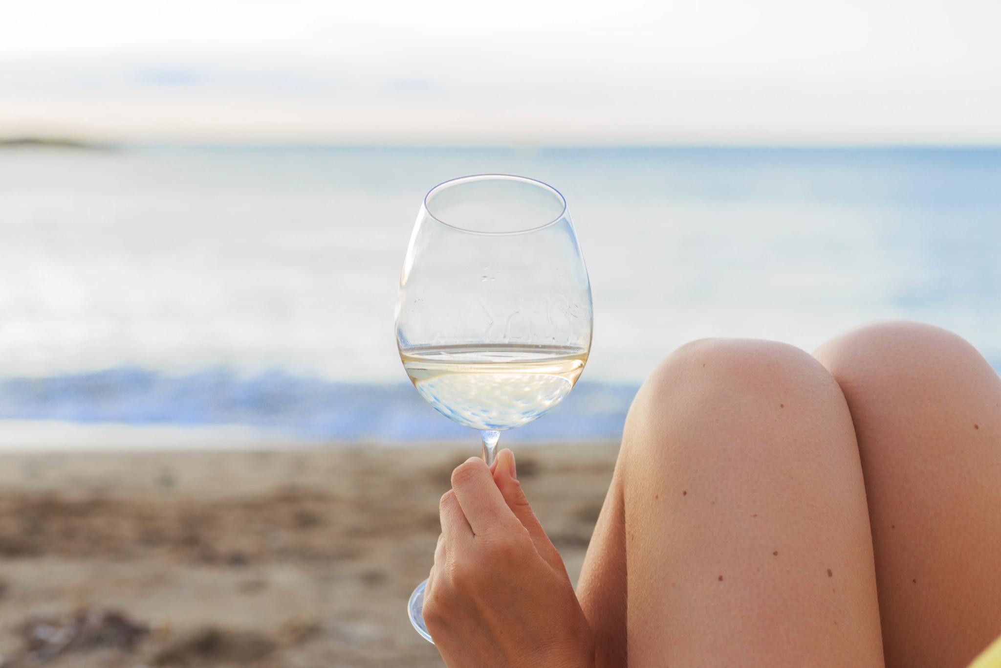 Femme tenant un verre de vin blanc à la plage avec vue sur la mer