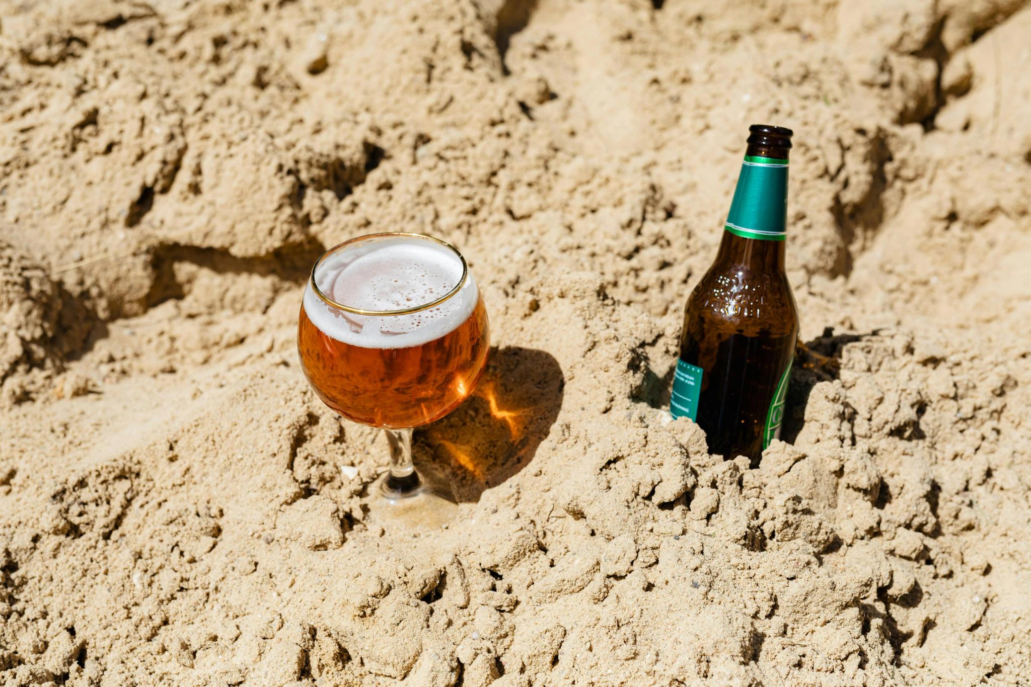 Verre de bière et bouteille sur le sable de la plage de Santa Giulia